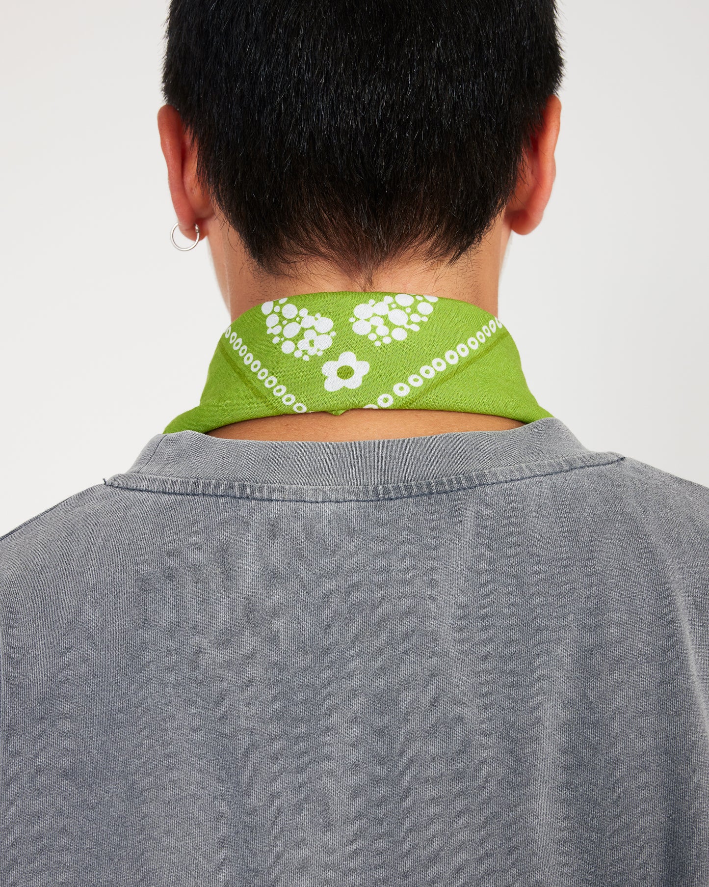 Person wearing a green bandana with white patterns around their neck against a plain background