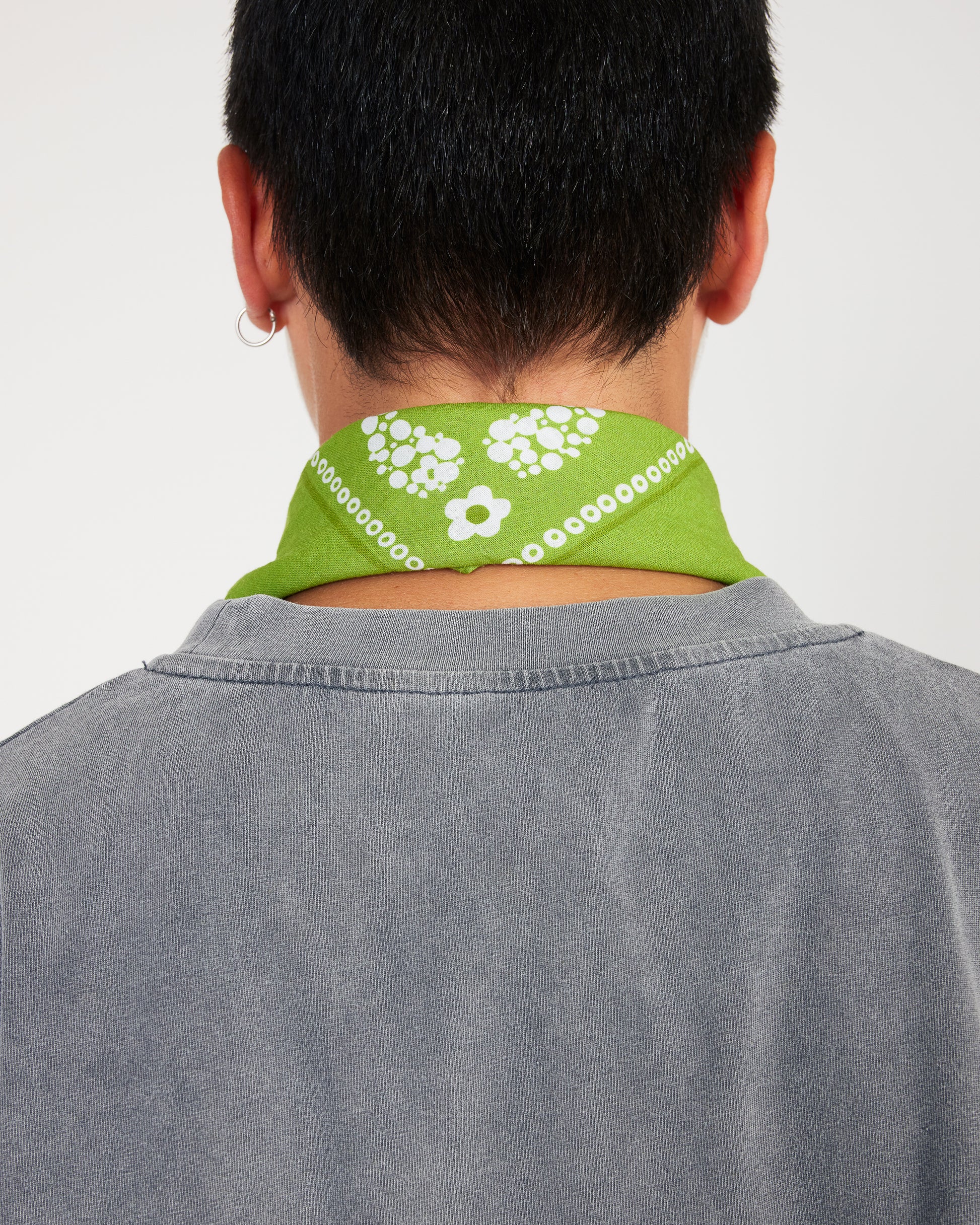 Person wearing a green bandana with white patterns around their neck against a plain background