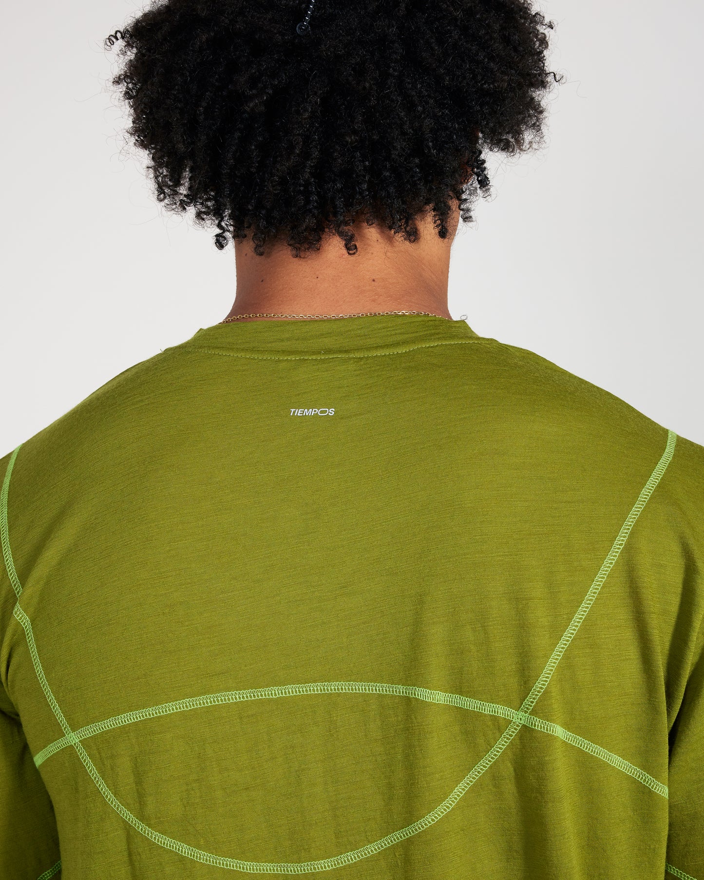 Person wearing a green athletic shirt with a brand logo on the back against a white background