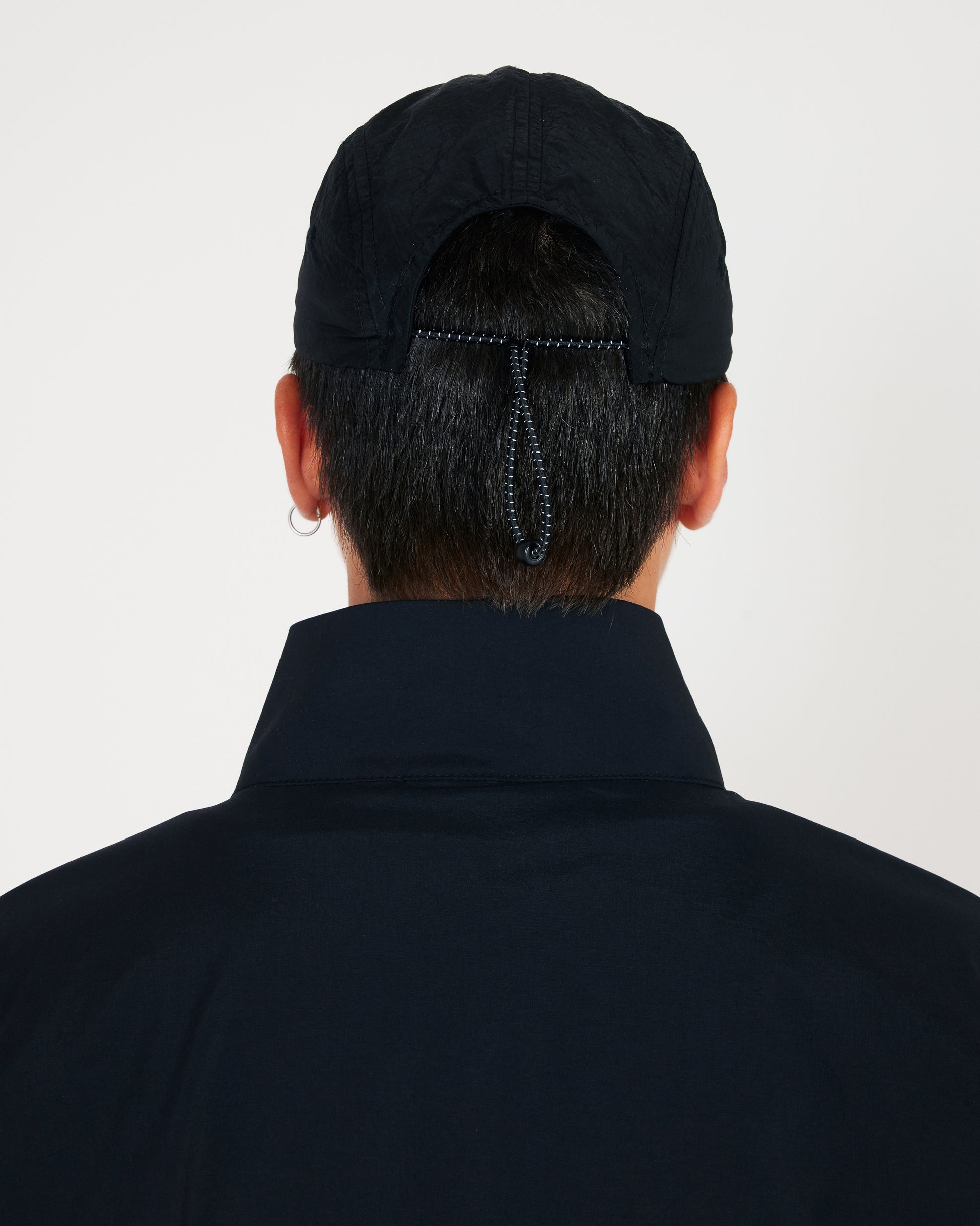 Person wearing a black cap and dark jacket on a light gray background