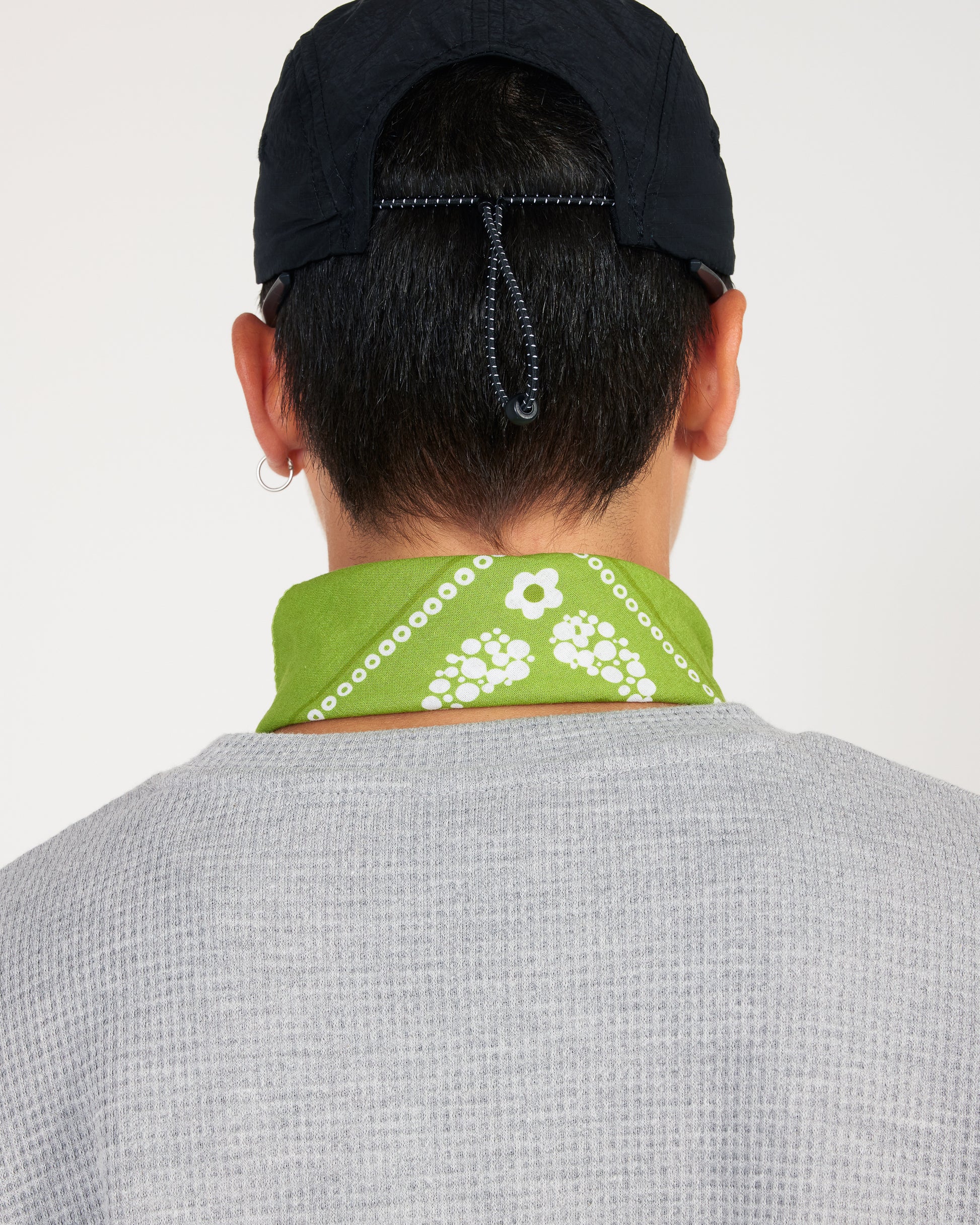 Person wearing a green bandana with white patterns around their neck, on a plain background