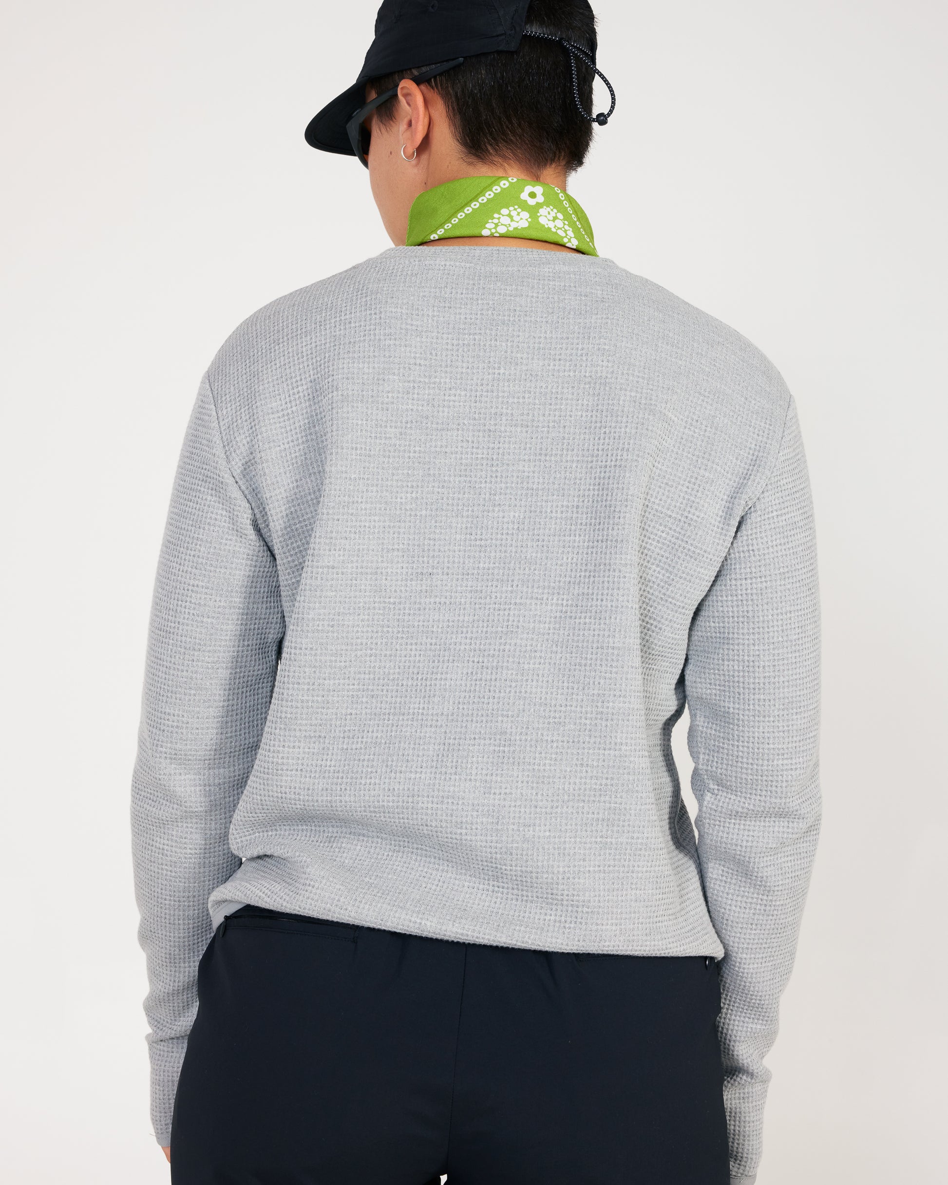 Person wearing a gray long-sleeve shirt and black pants with a green bandana around their neck on a white background