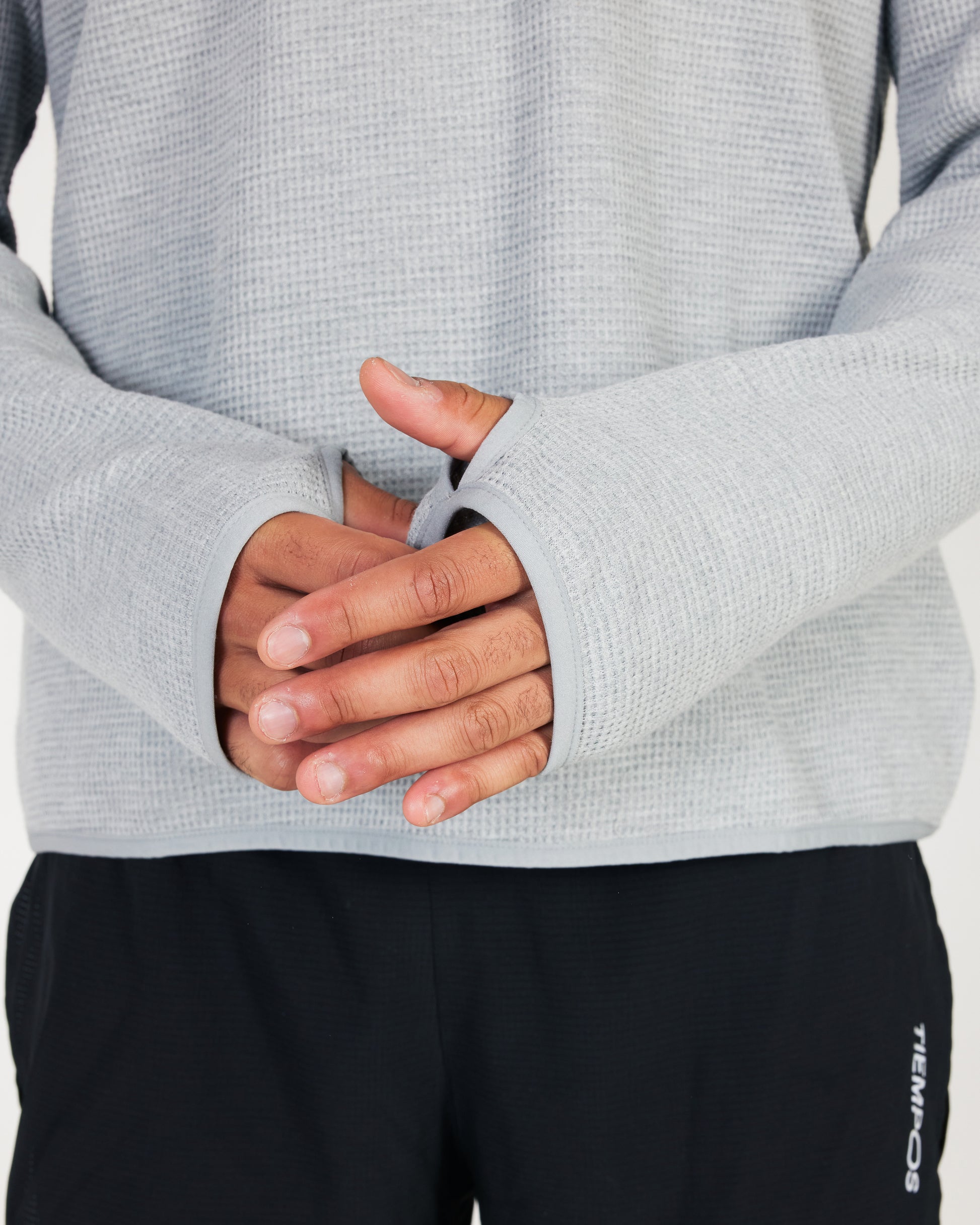 Close-up of a person wearing a gray textured sweater with black pants.