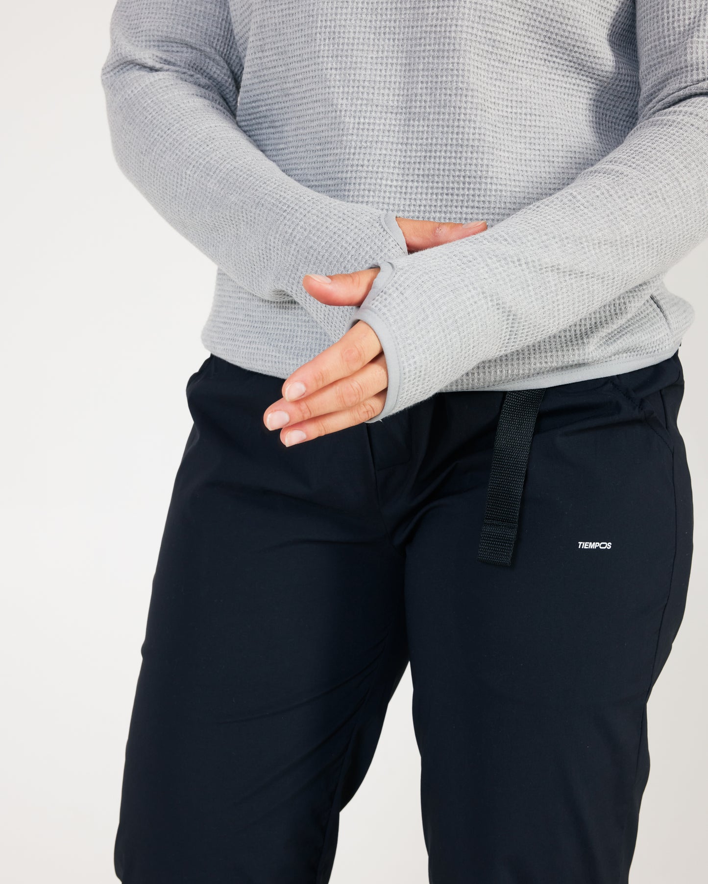 Person wearing a gray sweater and black pants with a visible brand logo on a light gray background