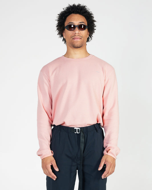 Man wearing a light pink sweater and dark pants on a white background