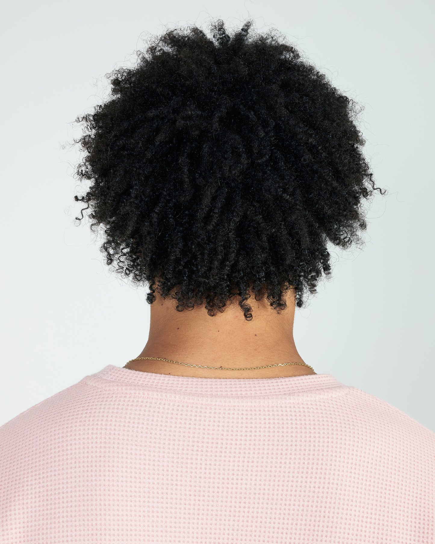 Person with textured black hair wearing a light pink shirt against a light gray background
