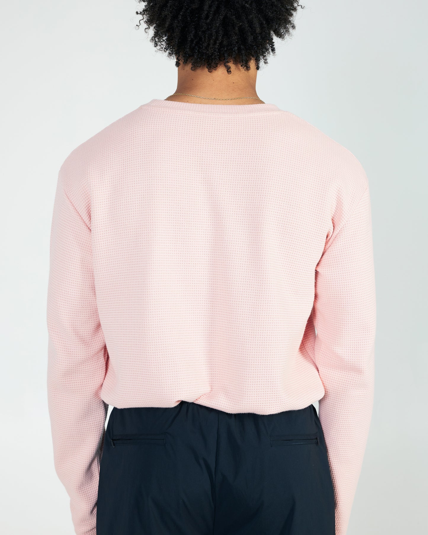 Person wearing a light pink long-sleeve shirt and dark pants on a plain background