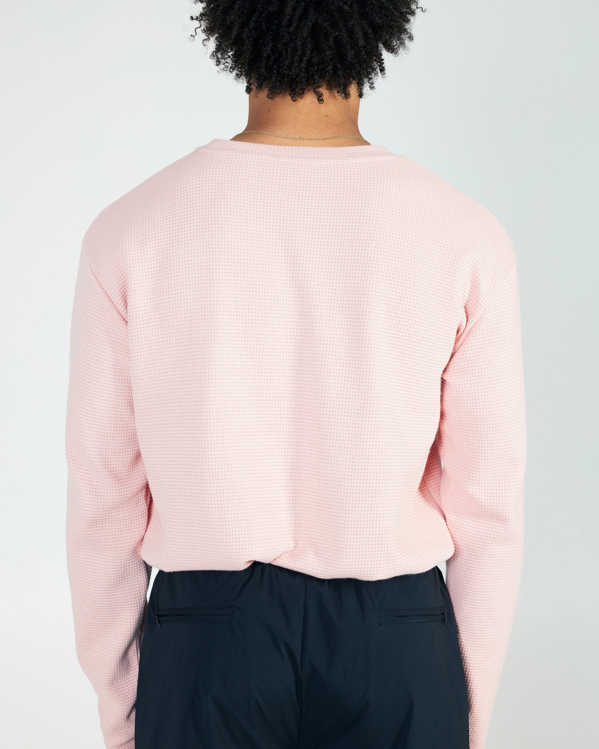 Person wearing a light pink long-sleeve shirt and dark pants on a plain background