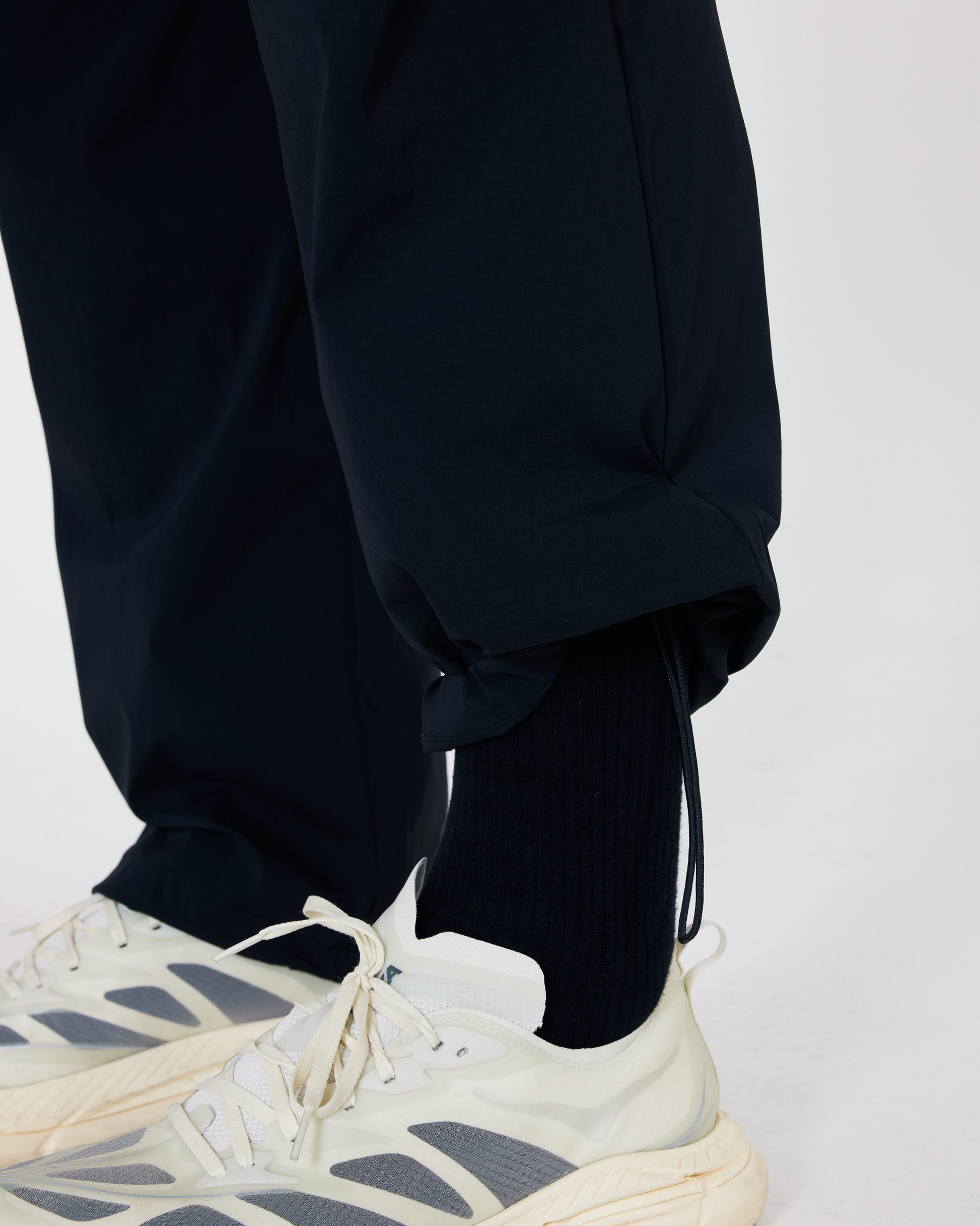 Person wearing black pants and white sneakers on a light gray background