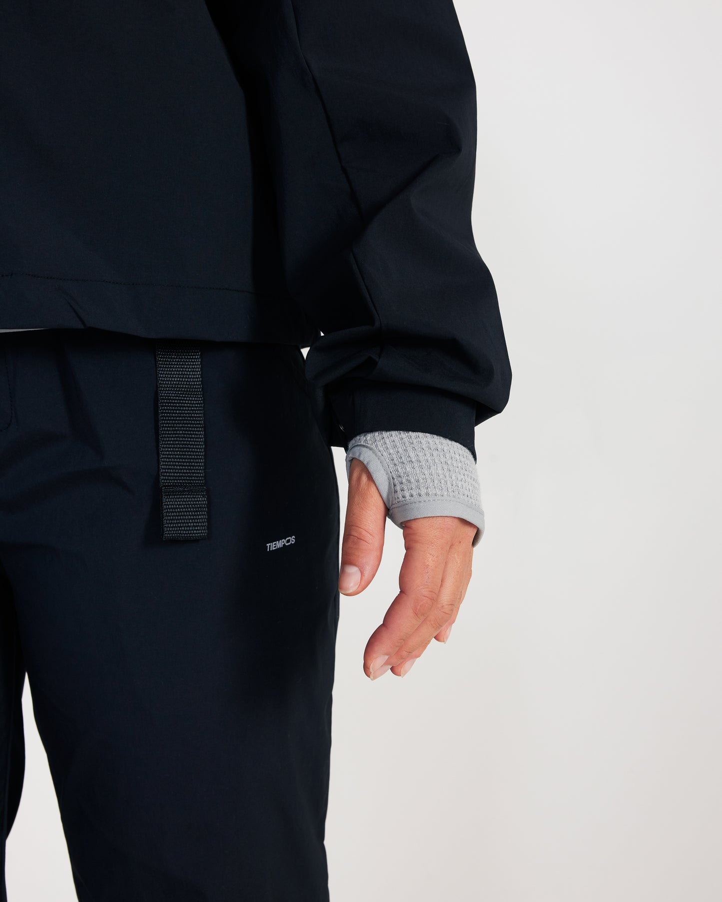 Person wearing a navy jacket and pants with a visible brand logo on a light gray background