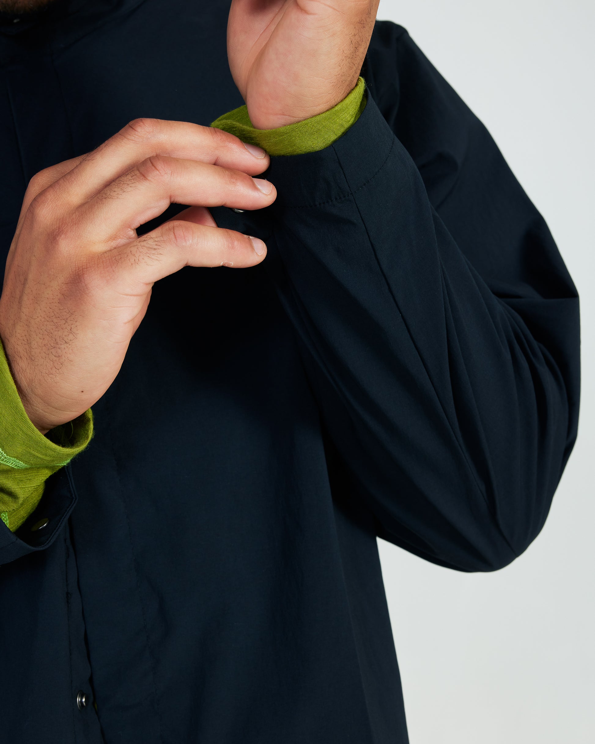 Person adjusting the collar of a dark jacket with green inner lining on a light gray background