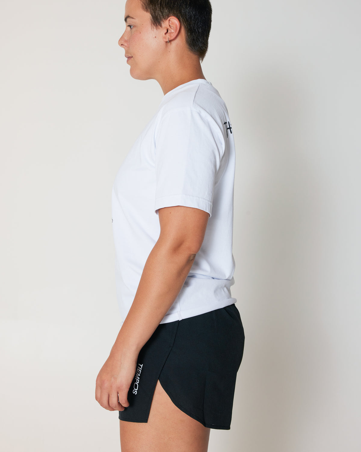 Person wearing a white t-shirt and black shorts with logos on a plain background