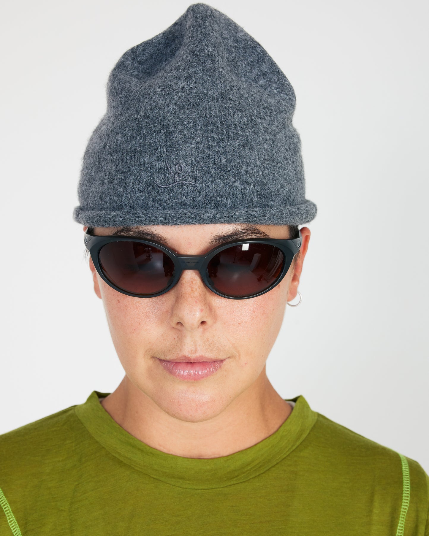 Person wearing a gray knit beanie and dark sunglasses on a white background
