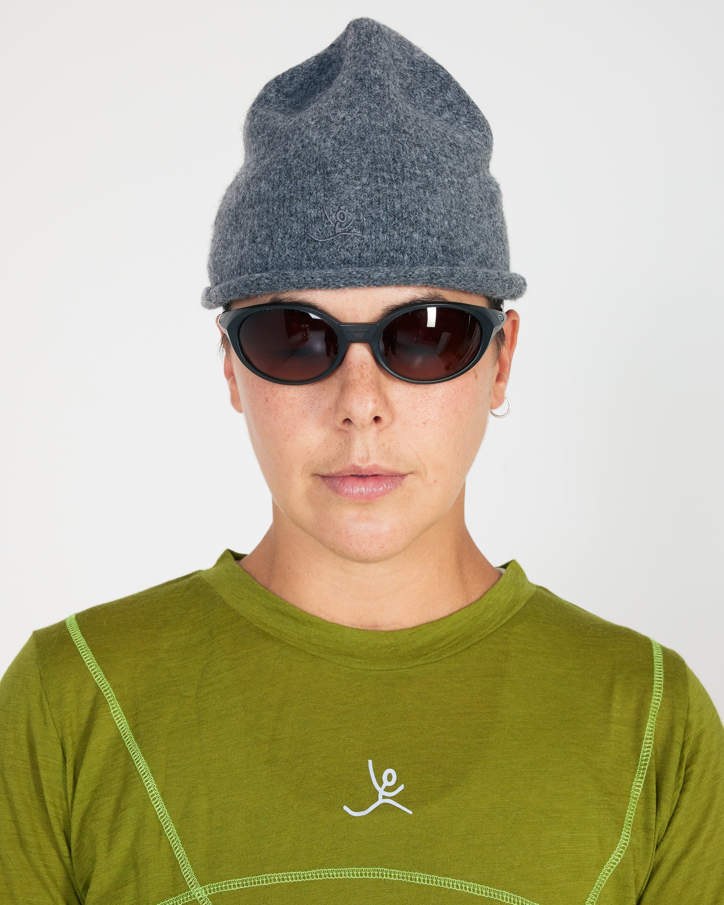 Person wearing a gray knit beanie and green shirt with a logo on a white background