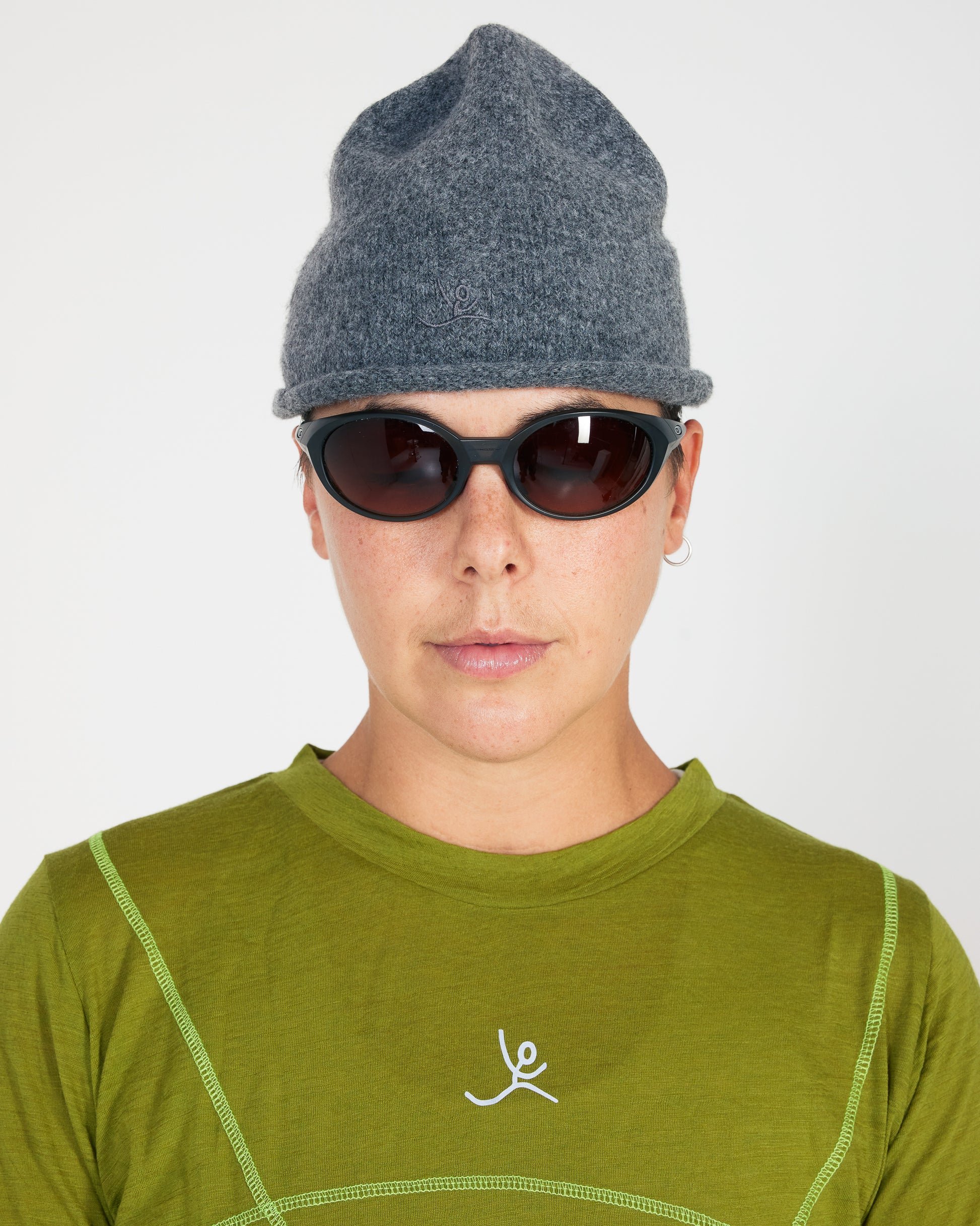 Person wearing a gray knit beanie and green shirt with a logo on a white background
