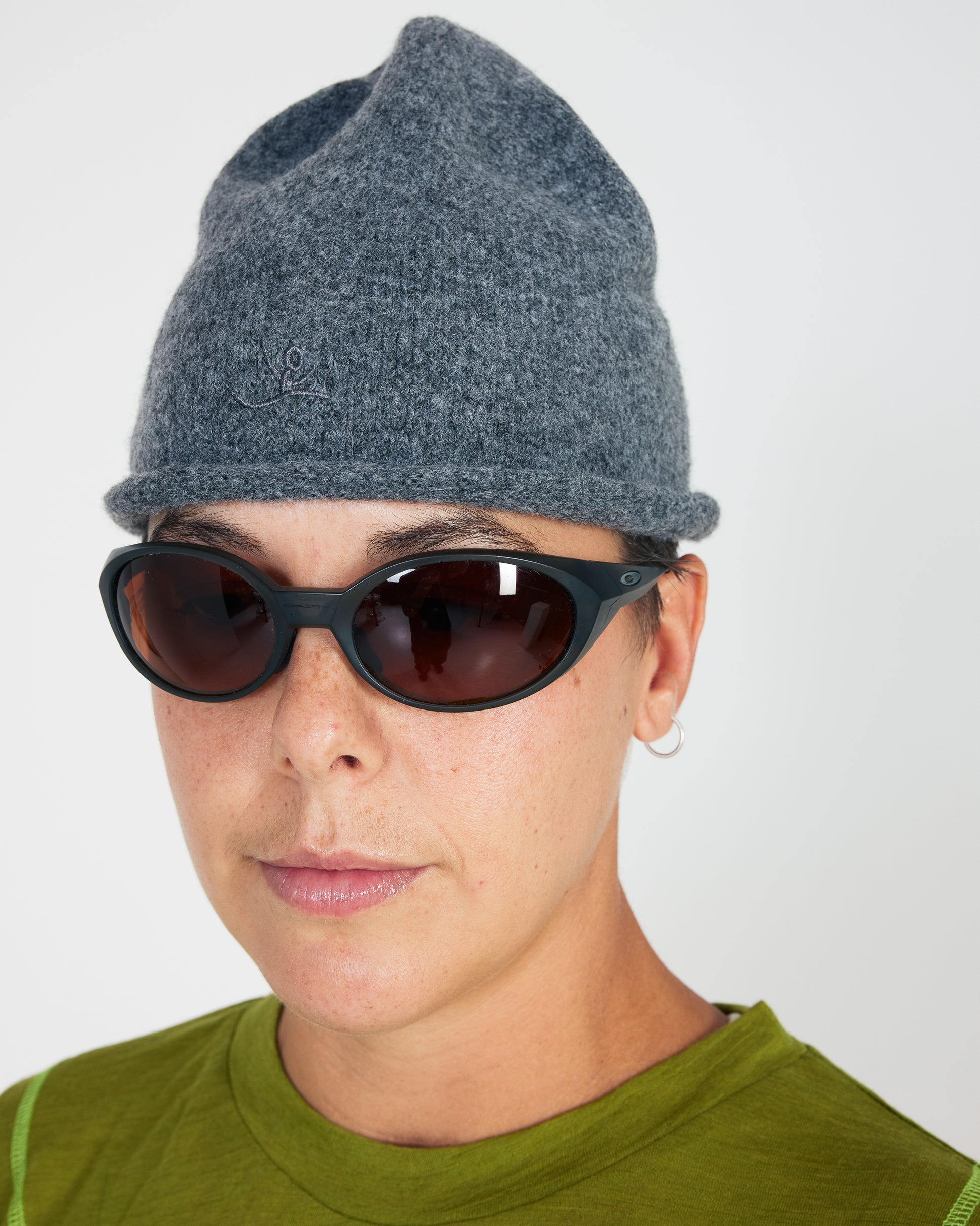 Person wearing a gray knit beanie and dark sunglasses on a plain background