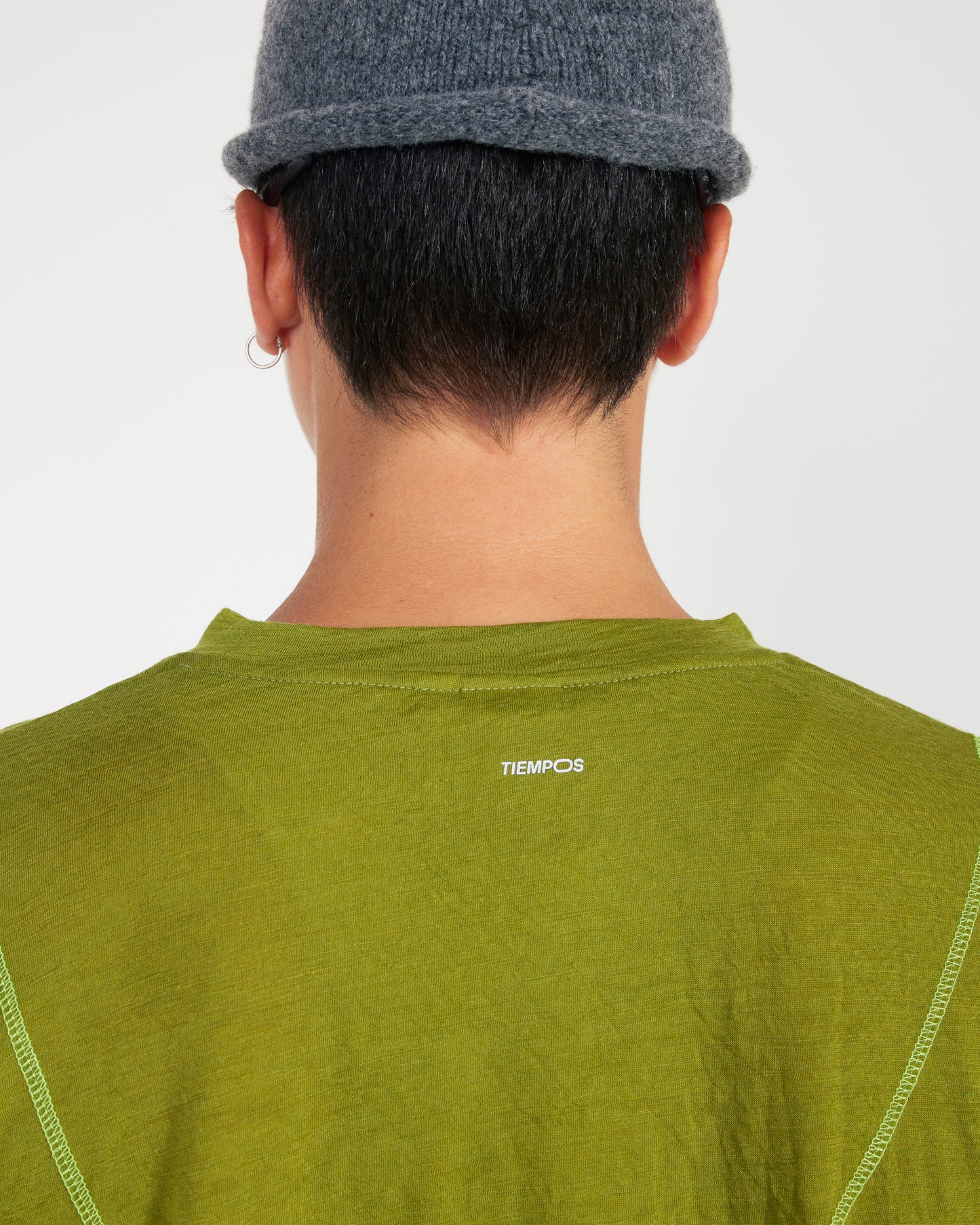 Person wearing a green shirt with 'TIEMPOS' logo on a plain background