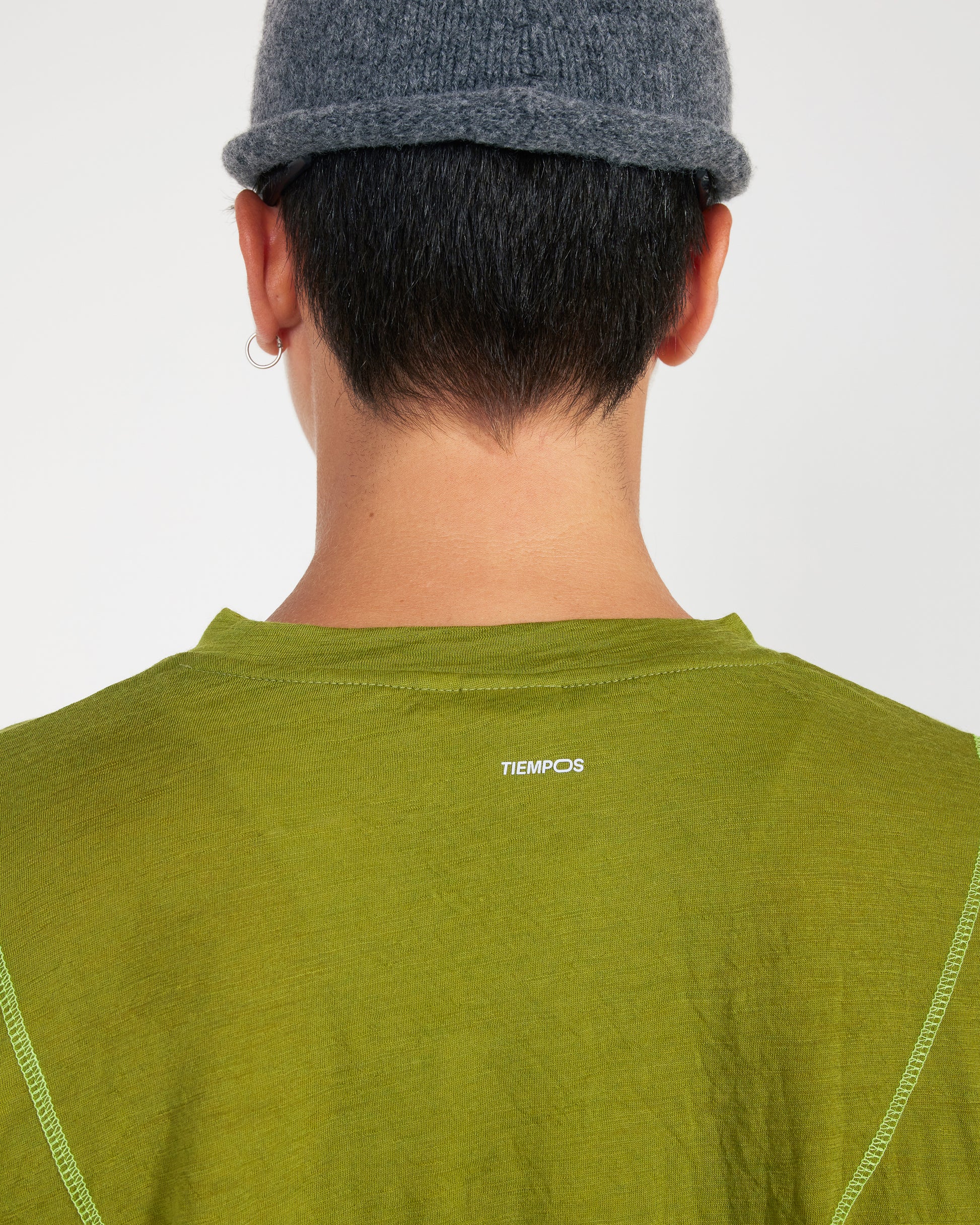 Person wearing a green shirt with 'TIEMPOS' logo on a plain background