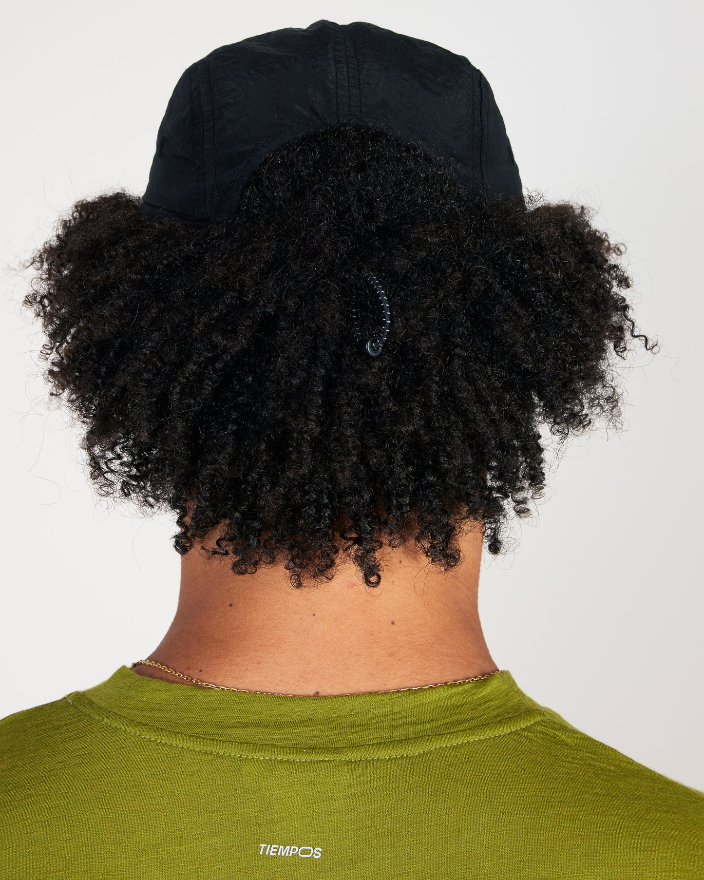 Person wearing a black cap and green shirt with 'Tiempos' branding on a white background