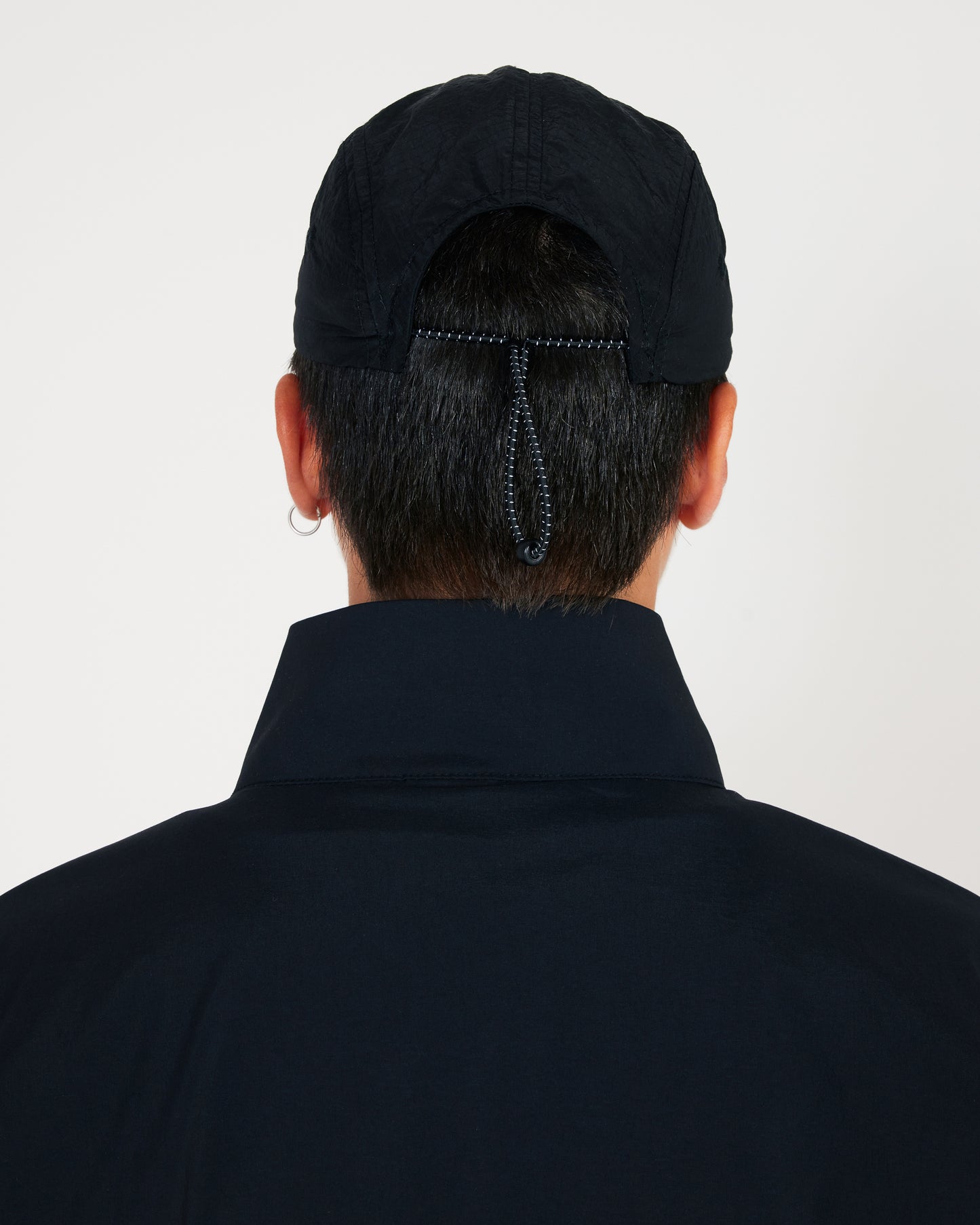 Person wearing a black cap and dark jacket on a light gray background