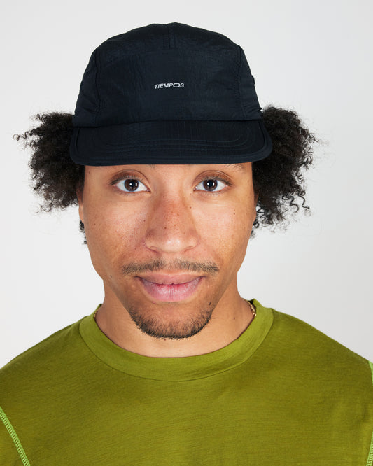 Person wearing a black cap with 'TIEMPOS' branding on a white background
