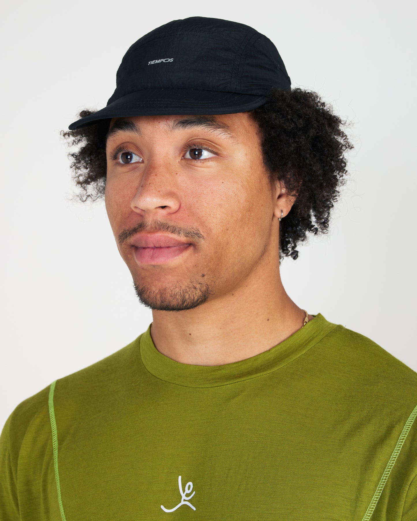 Man wearing a black cap and green shirt with a logo on a white background