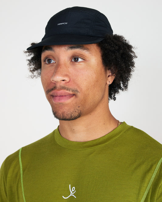 Man wearing a black cap and green shirt with a logo on a white background