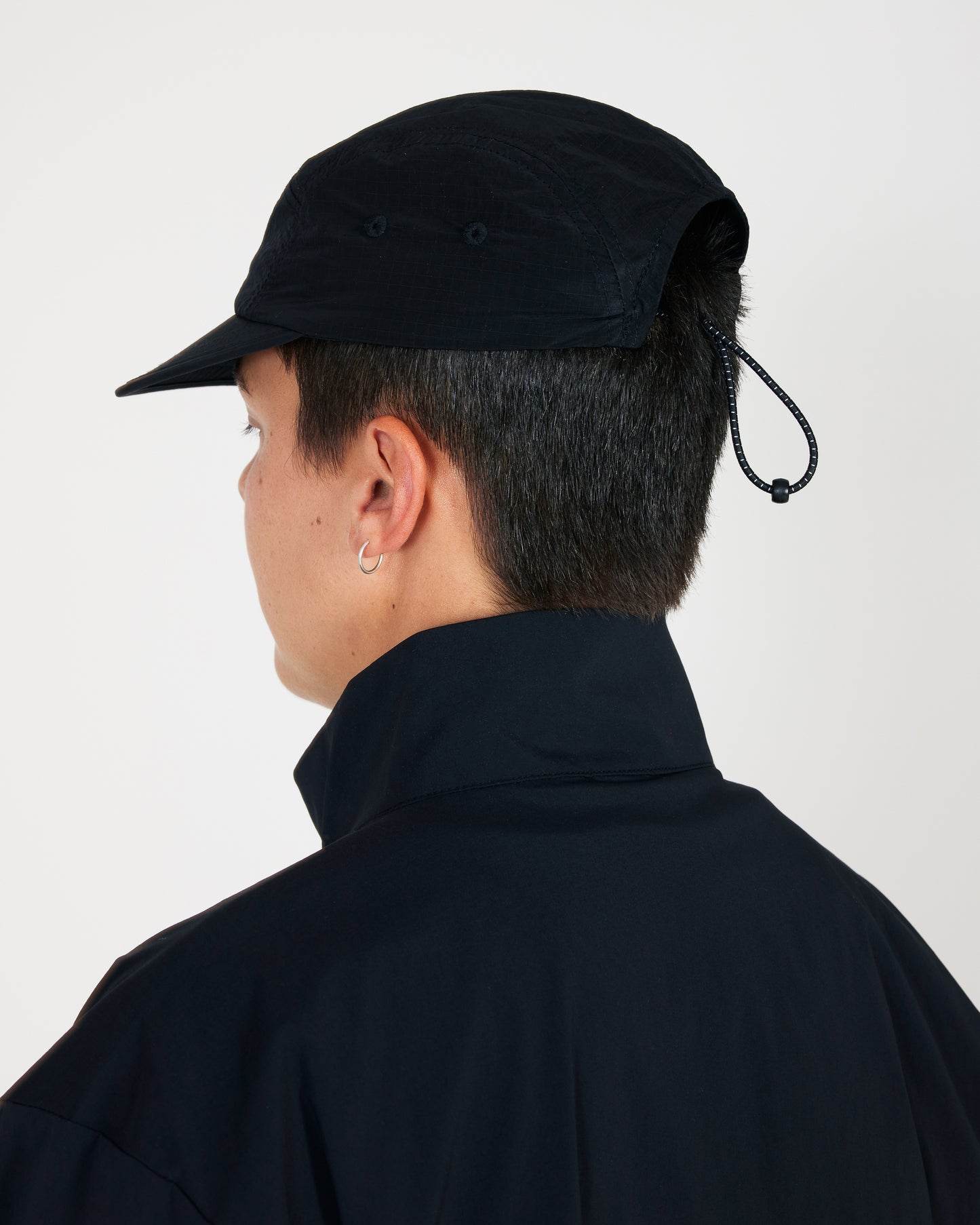 Person wearing a black cap with a drawstring on a plain background