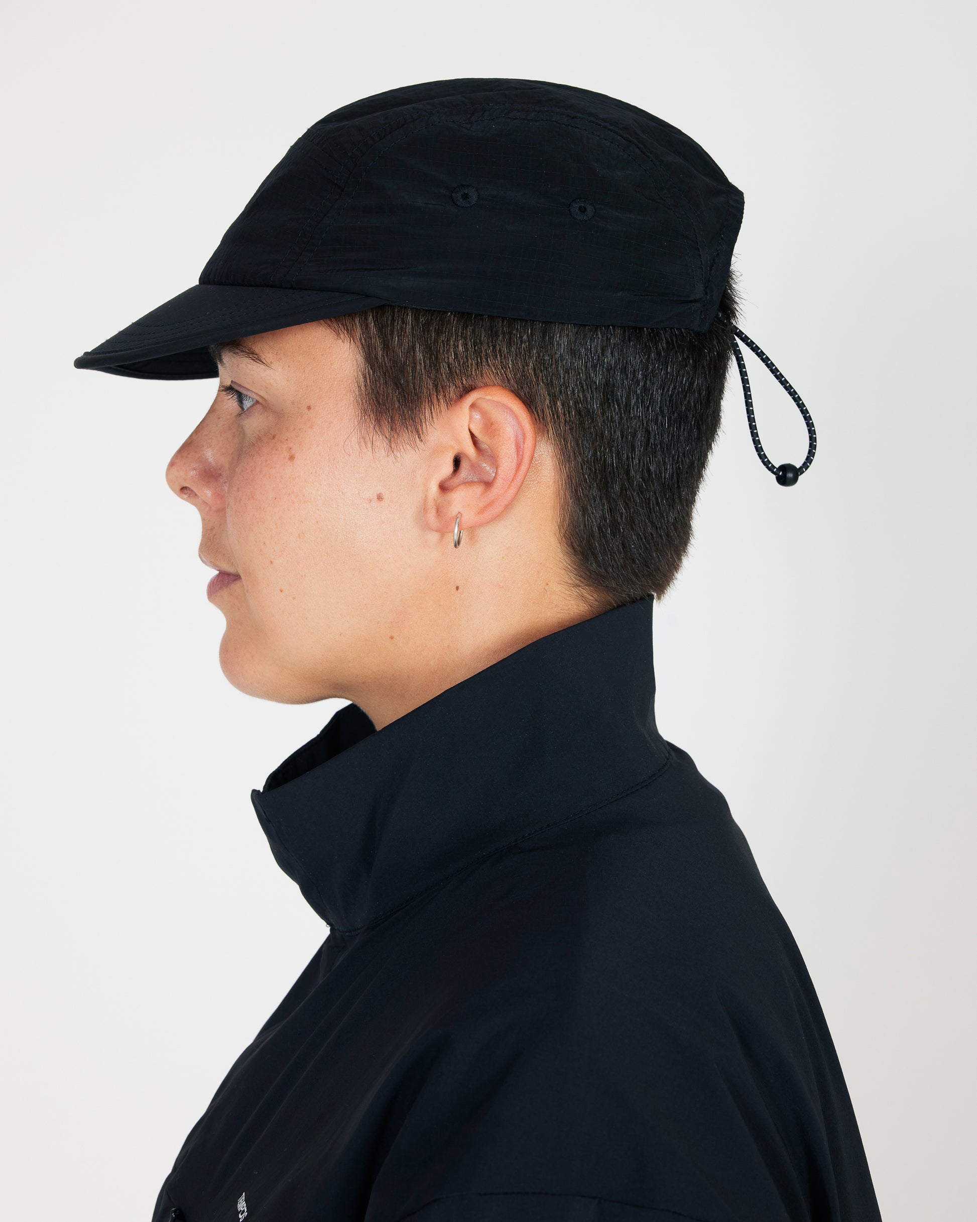 Person wearing a black cap and dark jacket against a light background