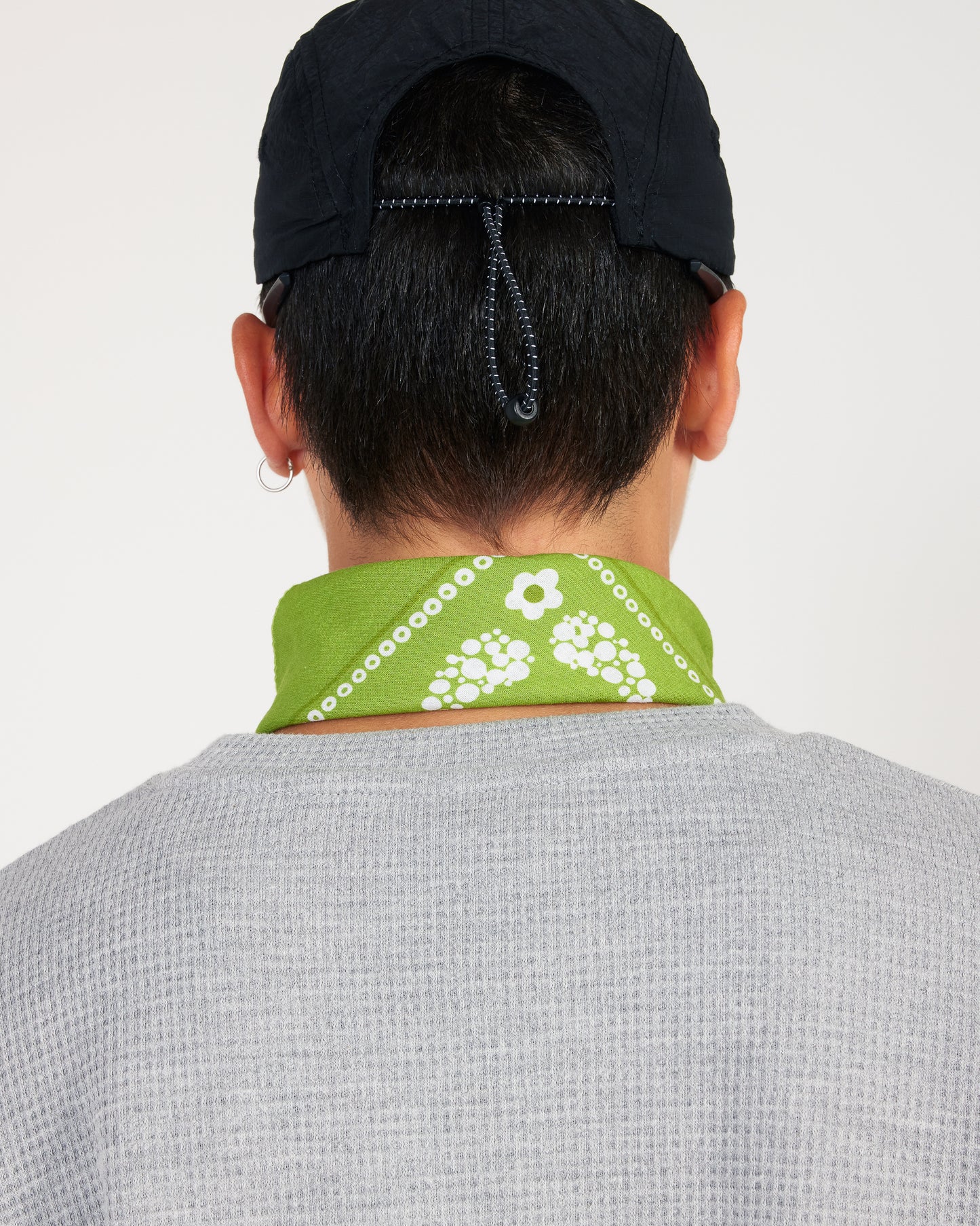 Person wearing a green bandana with white patterns around their neck, on a plain background