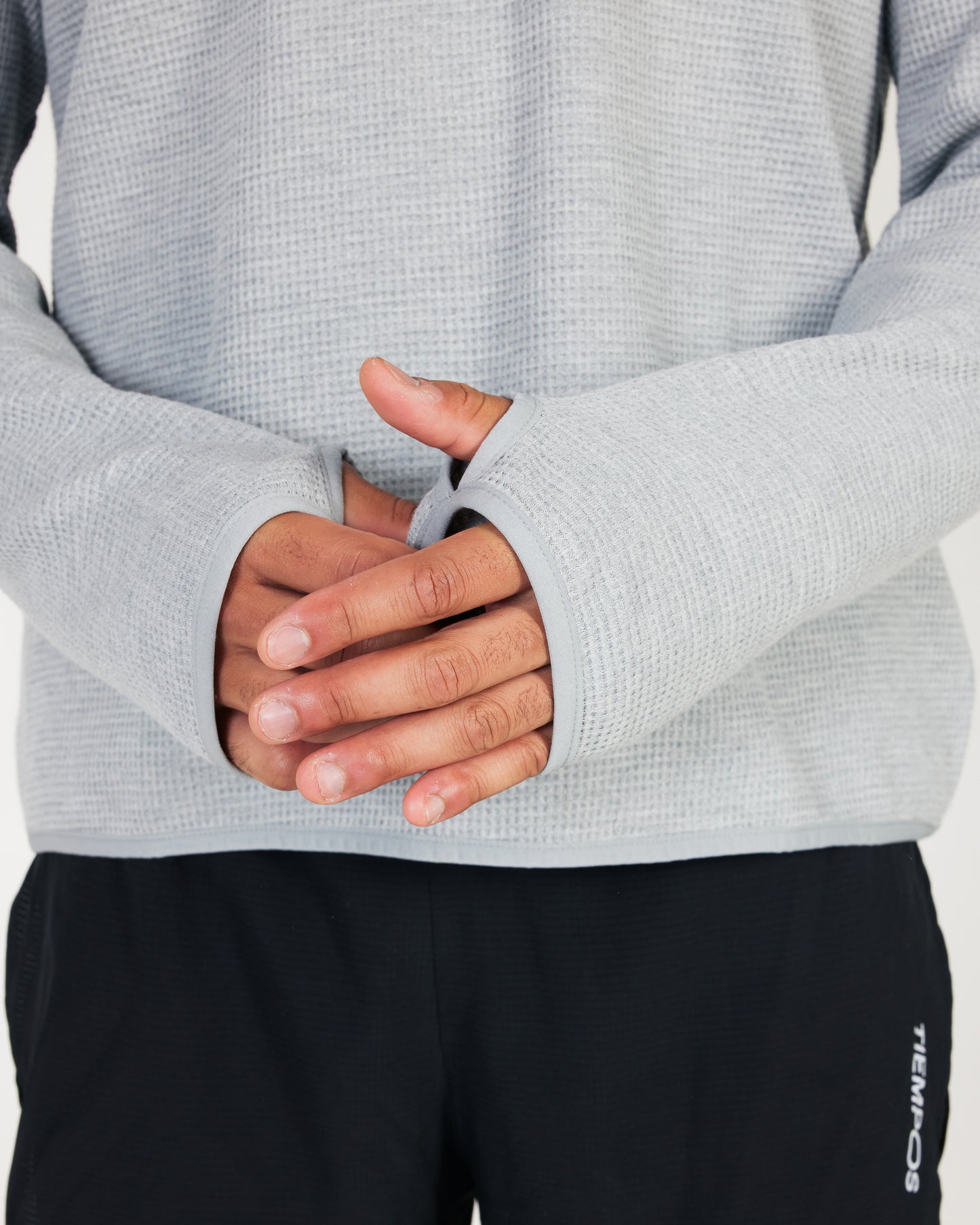 Close-up of a person wearing a gray textured sweater with black pants.