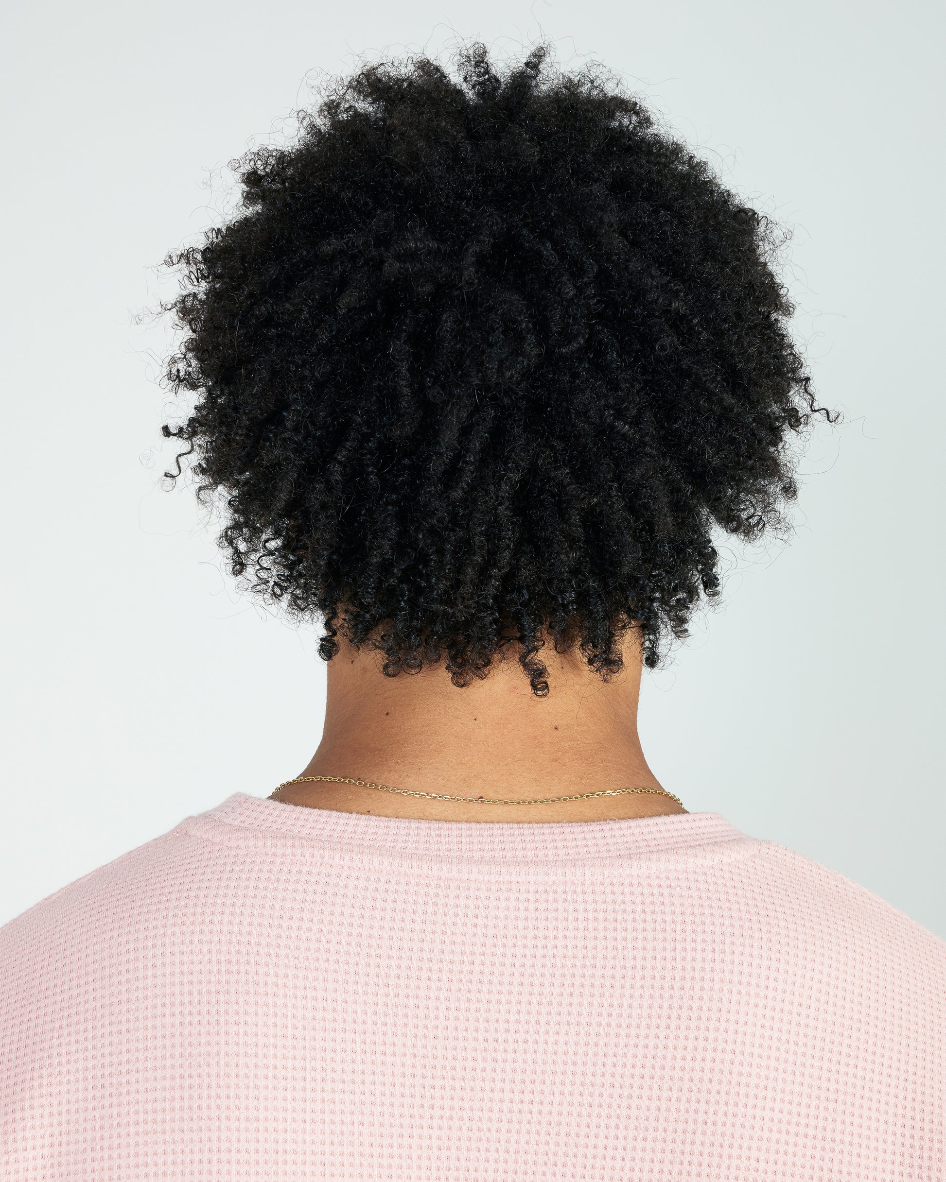 Person with textured black hair wearing a light pink shirt against a light gray background