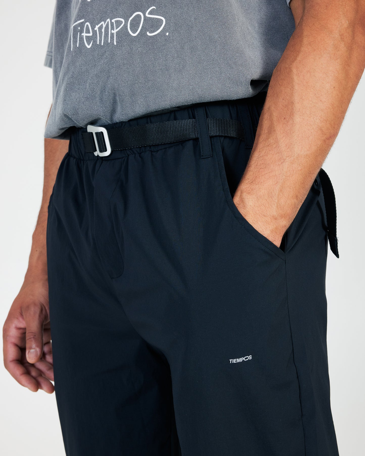 Person wearing black pants with a visible brand logo on a plain background