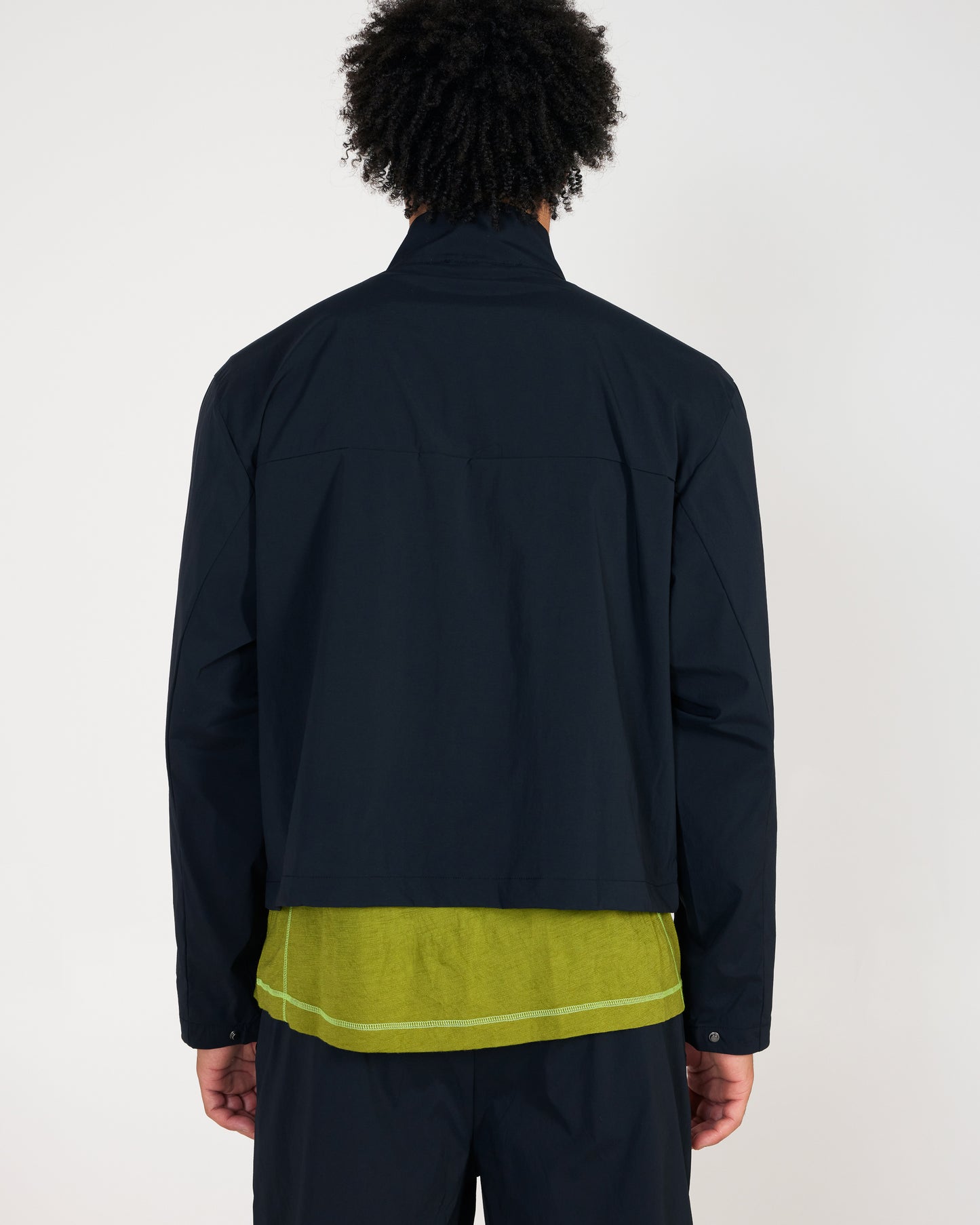 Person wearing a dark jacket over a green shirt on a plain background