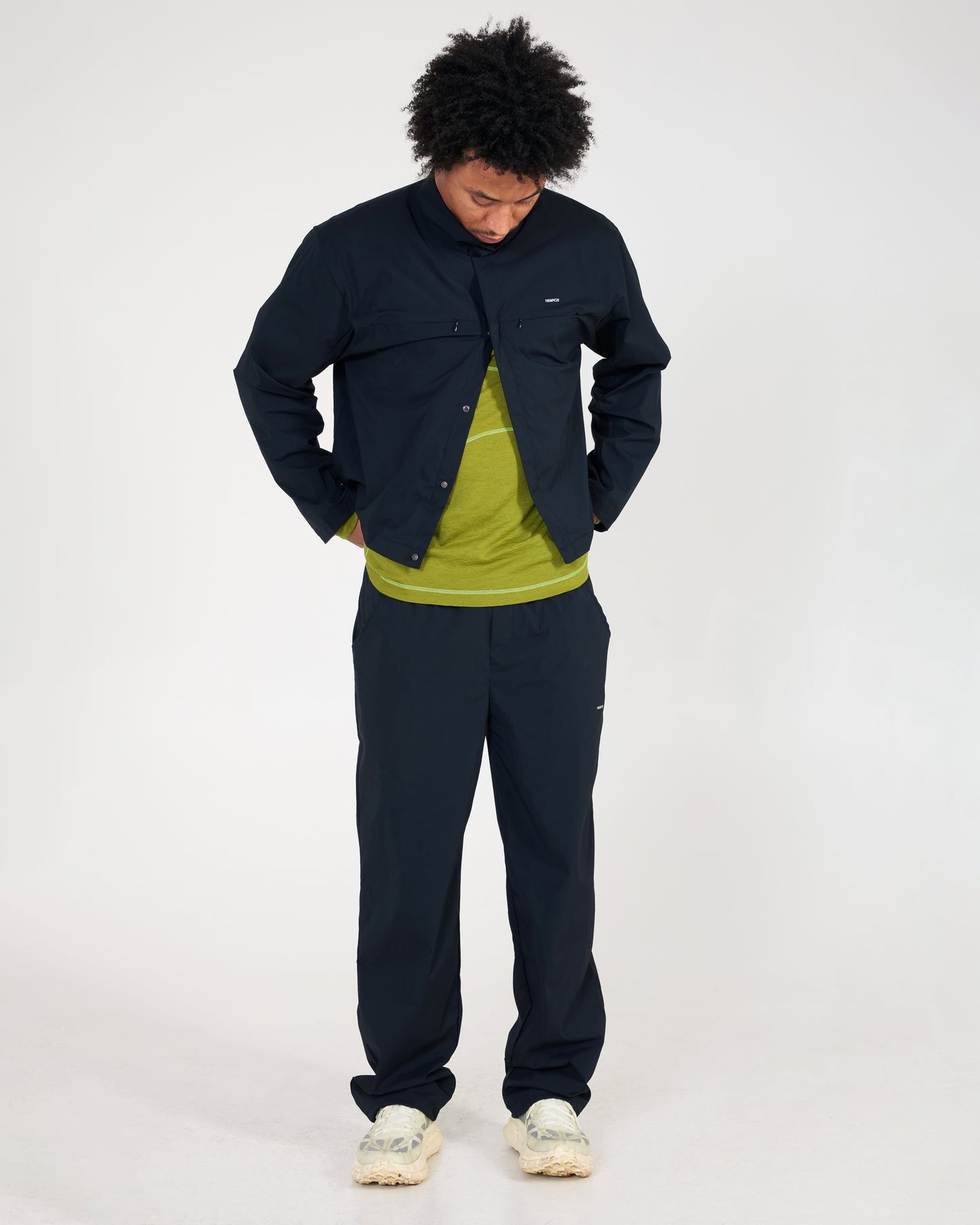 Person wearing a black jacket and pants with a green shirt on a white background