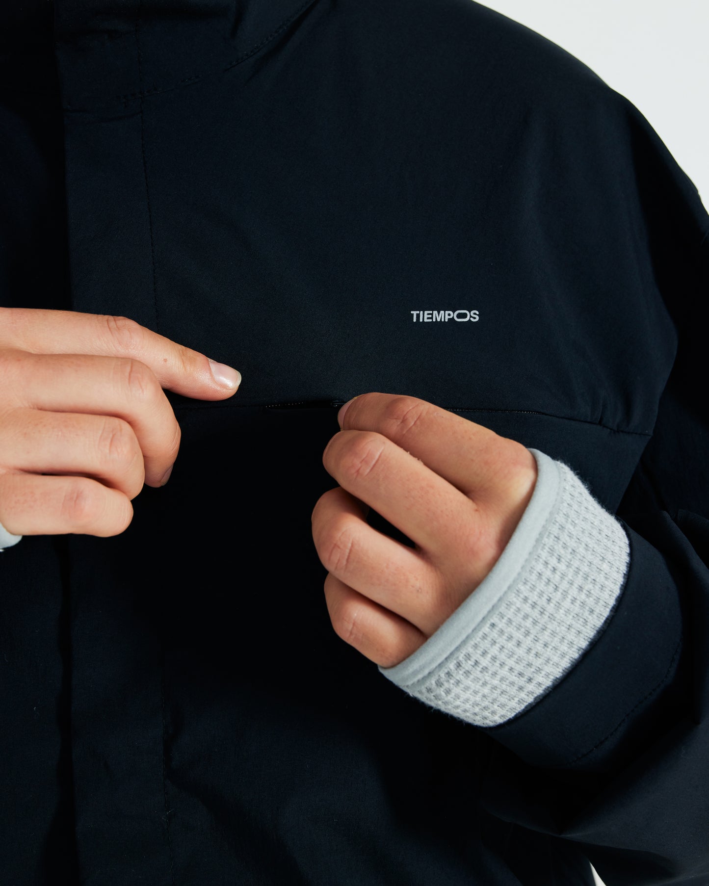 Person wearing a dark jacket with a white cuff, pointing to the brand 'Tiempos' on the chest.