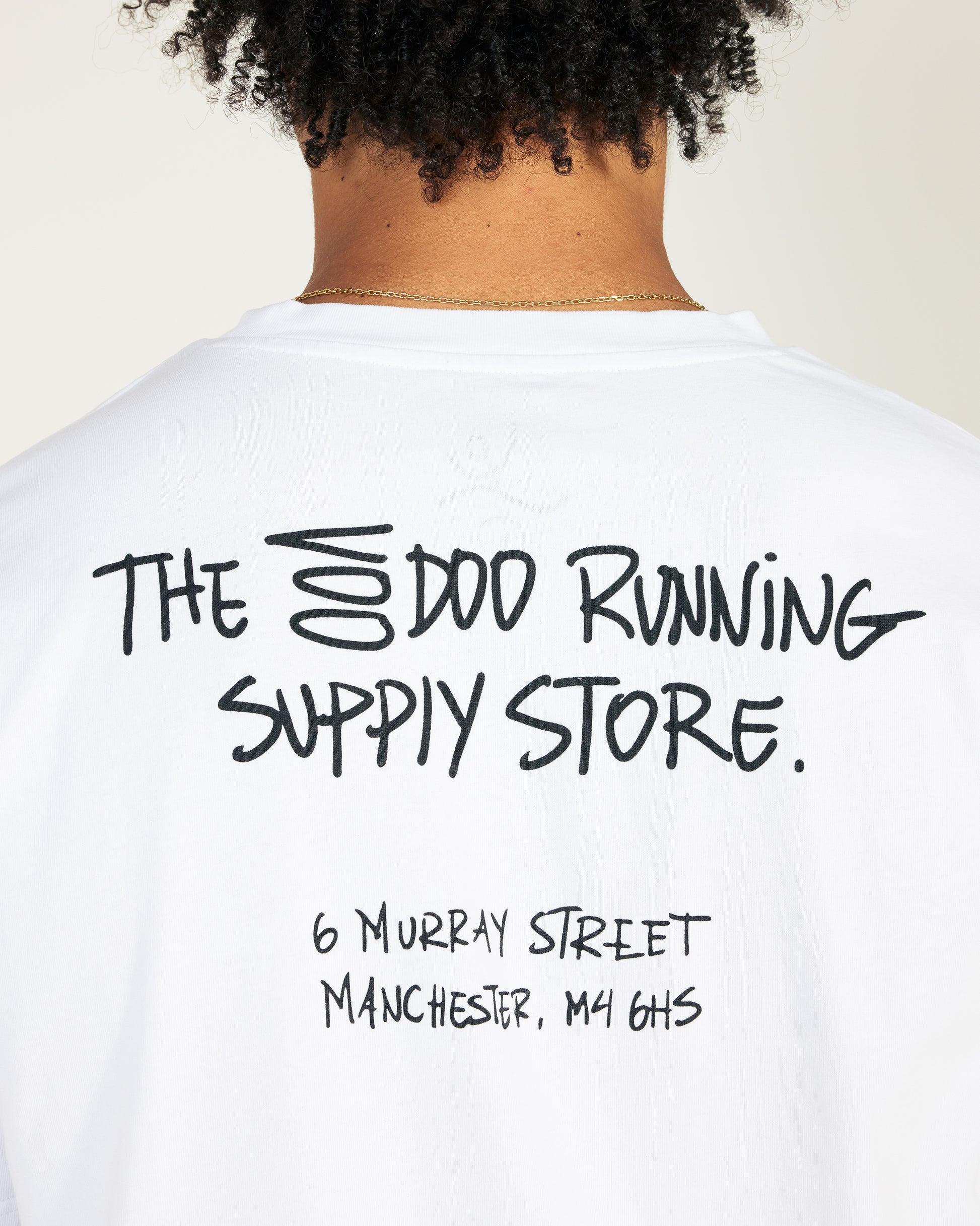 White t-shirt with black text on the back, featuring a store name and address.