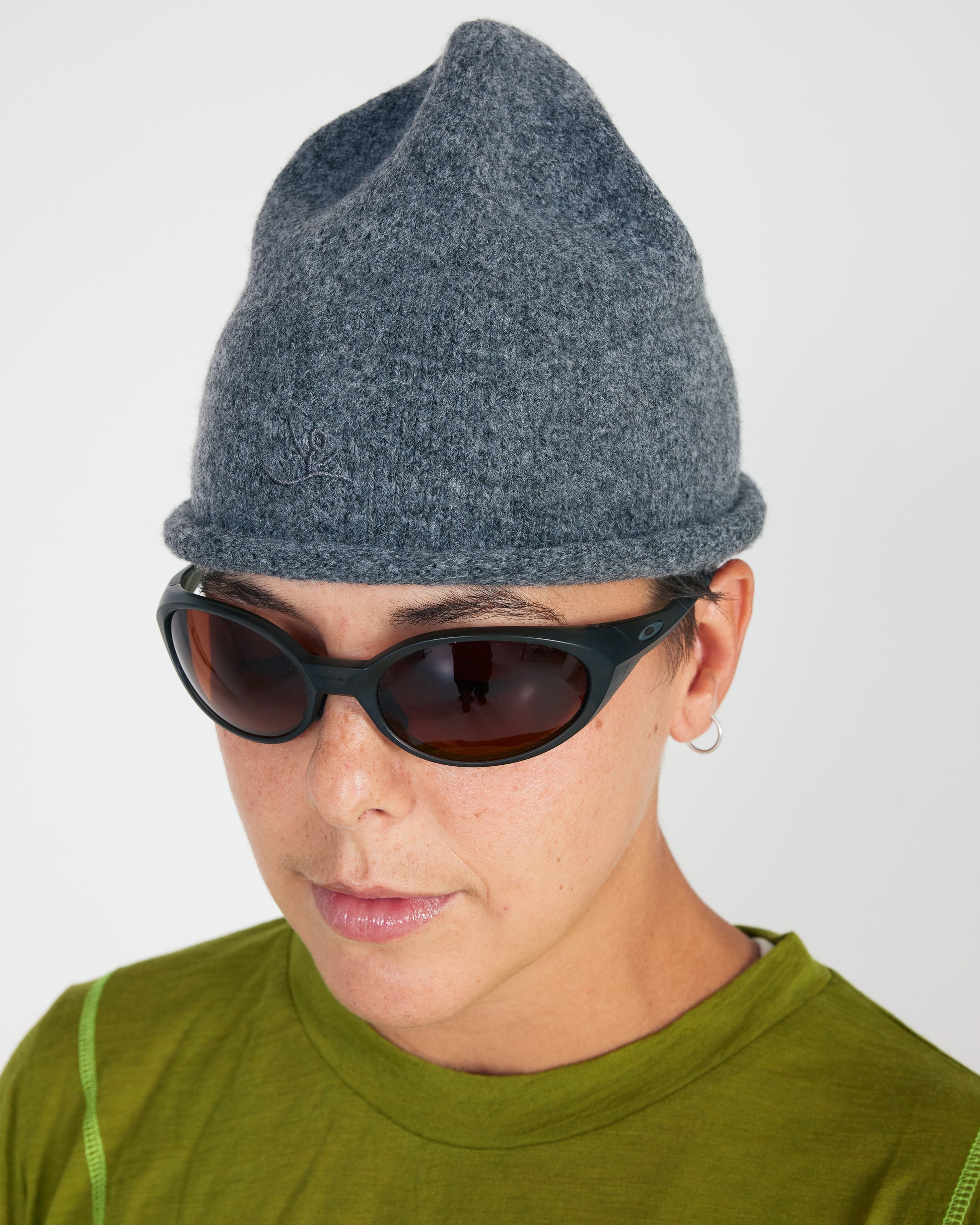 Person wearing a gray knit beanie and sunglasses on a plain background