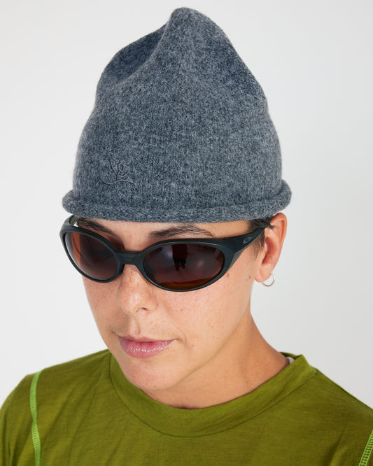 Person wearing a gray knit beanie and sunglasses on a plain background