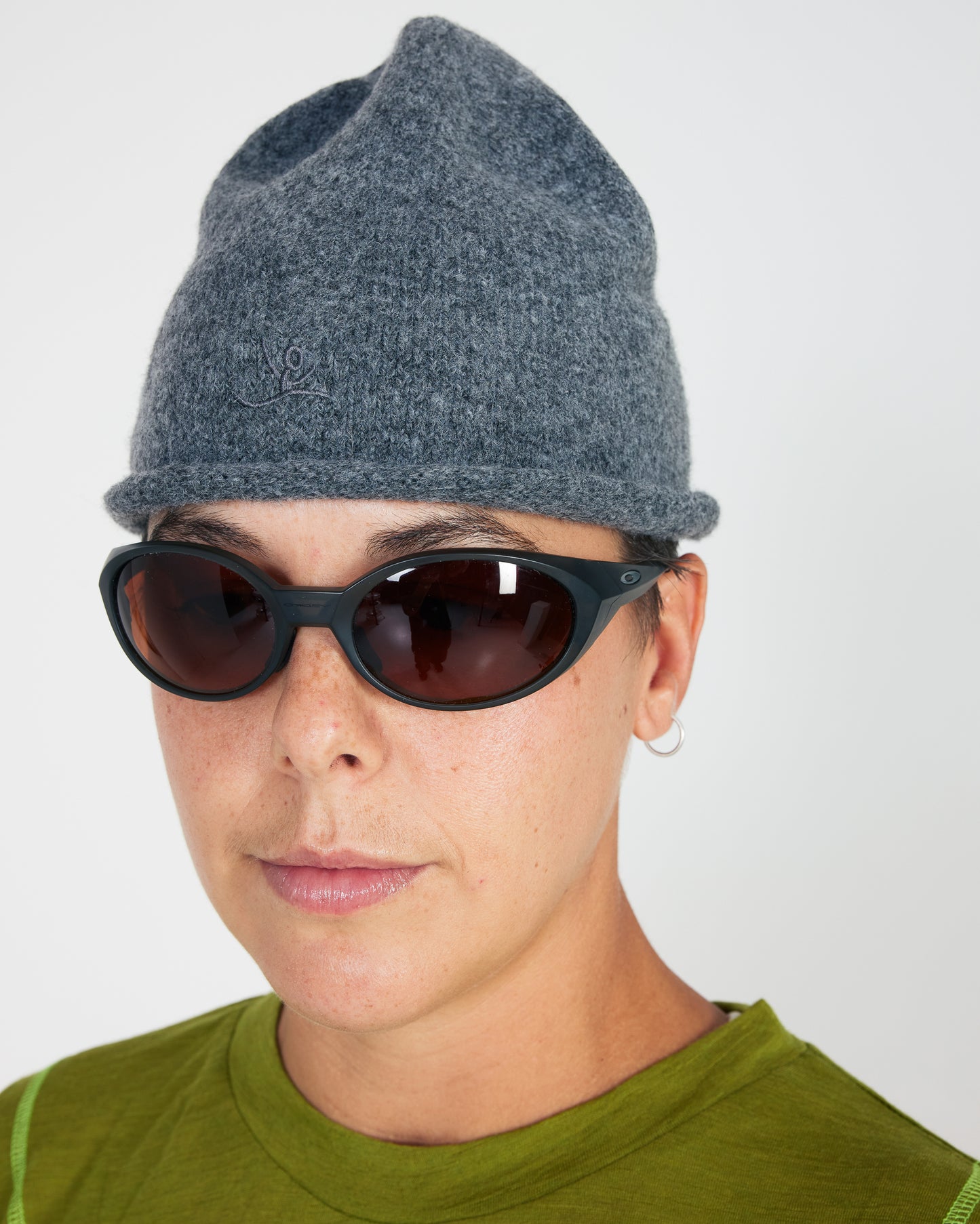 Person wearing a gray knit beanie and dark sunglasses on a plain background